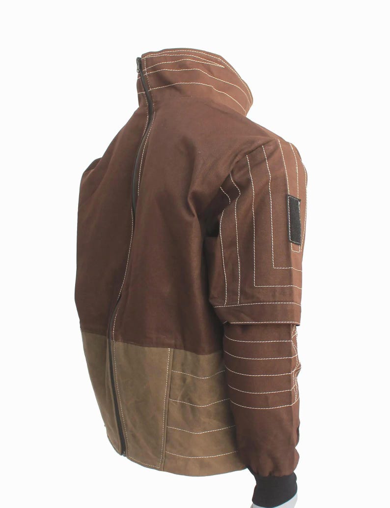May include: A brown jacket featuring a high collar, a full-length back zipper, and a lighter brown lower panel. The sleeves are detailed with horizontal white topstitching and a black rectangular patch on the upper arm, finished with black cuffs.