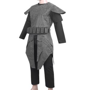 May include: A dark gray textured tunic with shoulder pauldrons and a matching waist belt featuring multiple rectangular pouches. The garment is worn over a black long-sleeved shirt and black trousers with ribbed detailing on the upper thigh area.
