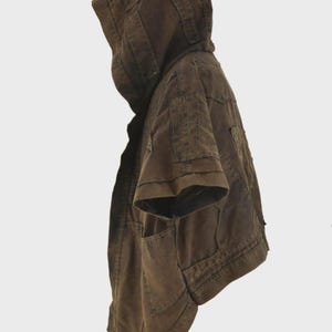 Puede incluir: Chaqueta con capucha marr&oacute;n con mangas cortas. La chaqueta tiene m&uacute;ltiples bolsillos y una capucha estructurada. La tela parece ser un material duradero, posiblemente similar a la lona. La chaqueta tiene un dise&ntilde;o utilitario.