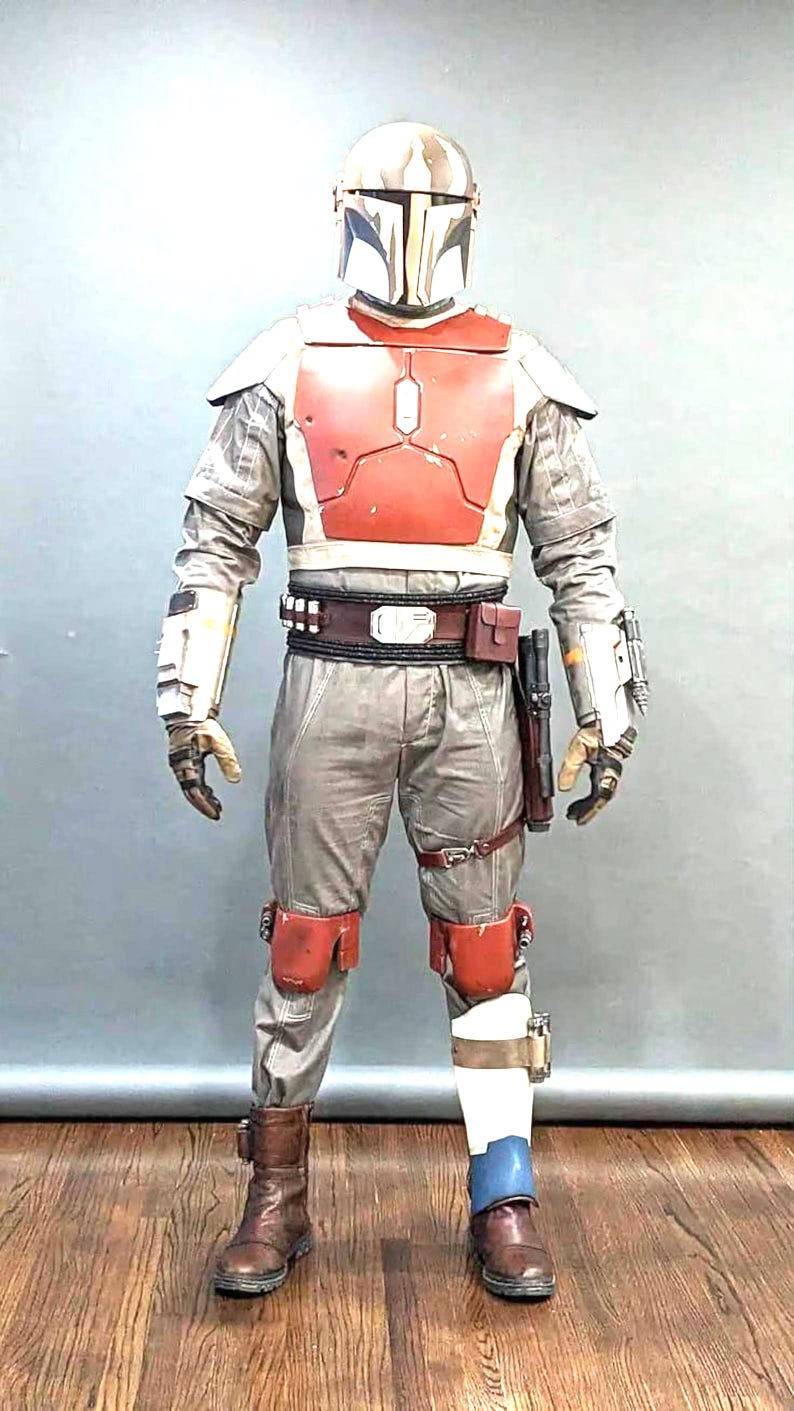 May include: A Mandalorian warrior costume. The outfit includes a helmet, chest armour, and protective elements in grey, red, and brown. The boots are brown, and the costume features a utility belt and holster. Measurements are in cm and kg.