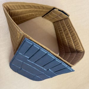 以下が含まれることがあります： 茶色のパッド入りカラーと、濃い灰色のテクスチャードプレート。 カラーは長方形のパターンでキルティングされています。 プレートは幾何学模様です。 カラーには黒いベルクロ留めが付いています。