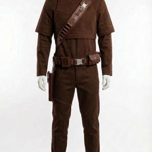 May include: A brown costume displayed on a mannequin. The outfit includes a high-collared top, pants, a belt with pouches, a shoulder strap, and a holster. The boots are brown. The costume is made of a suede-like material.