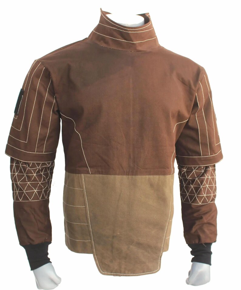 May include: A brown long-sleeve shirt featuring a high collar, a lighter brown lower panel, and white topstitching. The sleeves have a geometric triangular pattern on the forearms, while the cuffs are black. The garment has a structured design.