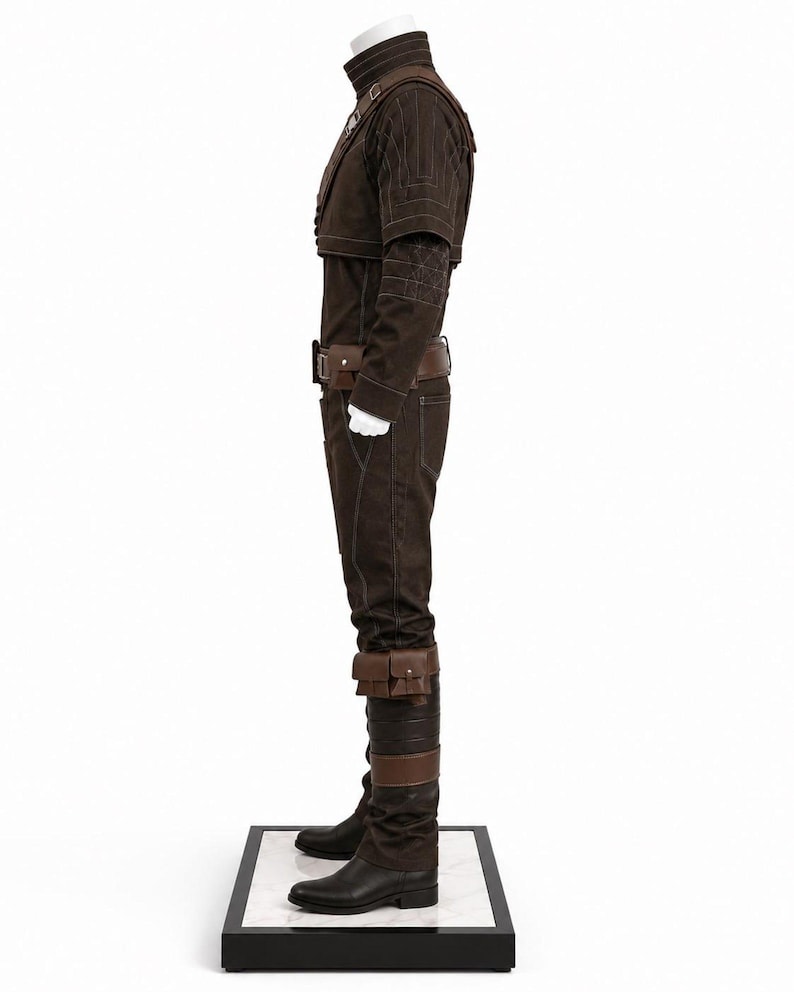 May include: A brown costume displayed on a white mannequin. The outfit includes a jacket, pants, belt, and boots. The jacket has a high collar and decorative stitching. The pants have pockets and the boots are black. The costume is displayed on a black and white platform.