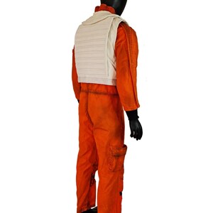 May include: A bright orange flight jumpsuit featuring a textured fabric, long sleeves with black cuffs, and a white quilted vest worn over the top. The jumpsuit includes a cargo pocket on the leg and a high collar, displayed on a black mannequin.