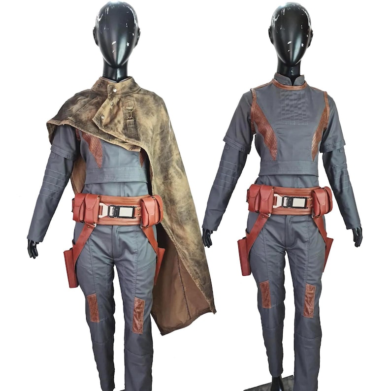 May include: Two dark gray jumpsuits featuring brown leather-like accents on the shoulders, knees, and waist belts with metallic buckles. One jumpsuit includes a distressed brown cape draped over the shoulder. Both outfits are displayed on black mannequins.