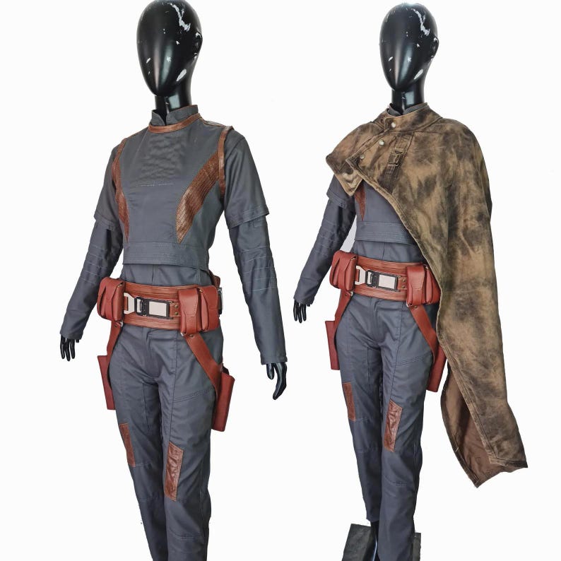 May include: Two dark gray jumpsuits with long sleeves and high collars, featuring brown textured accents on the shoulders and legs. Each outfit includes a brown utility belt with multiple pouches and a metallic buckle, plus a distressed brown cape.