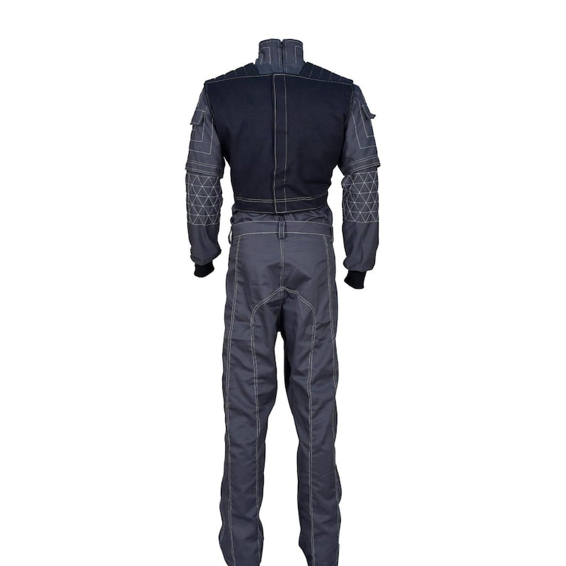 May include: A gray racing suit with a black upper section. The suit features white stitching, geometric patterns on the sleeves, and black cuffs. It has a high collar and multiple pockets, designed for professional racing.