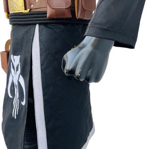 May include: Black quilted fabric costume with white accents and a brown leather belt. The belt has a gold buckle and brown pouches. A white emblem is on the black fabric.