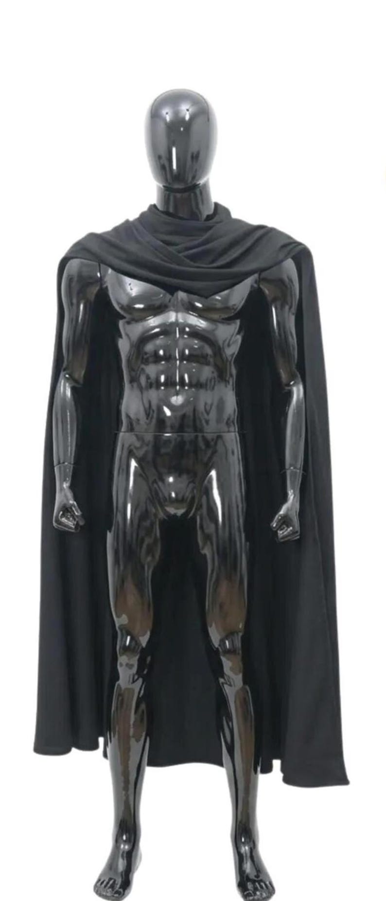 May include: A black mannequin with a glossy finish, wearing a black cape. The mannequin has a muscular physique and is standing against a white background. The cape drapes over the shoulders and arms.