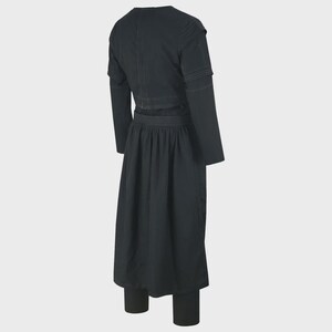 May include: A black outfit featuring a long-sleeved top with a V-neck and a long skirt. The top has a cropped design with a belt, and the skirt is pleated. The outfit is paired with matching black leggings. The stitching is visible in a lighter color.