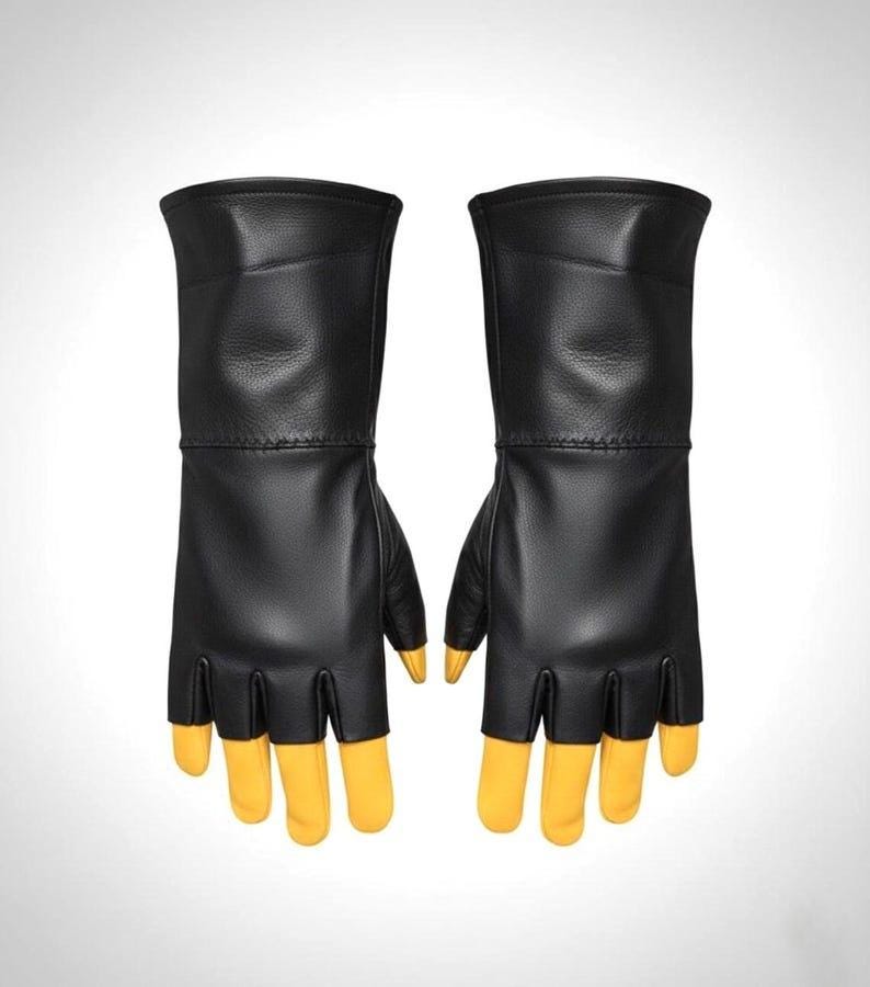 May include: A pair of fingerless gloves featuring black leather construction on the back of the hand and wrist, with contrasting yellow leather fingers that extend past the black leather cutouts. The gloves have a long cuff design.