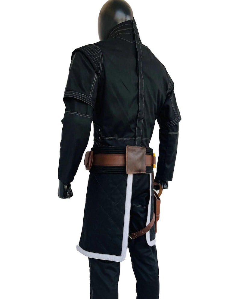 May include: Black costume with white stitching and accents. The outfit includes a long coat with a quilted design, a brown belt with pouches, and a holster. The costume has a high collar and long sleeves.