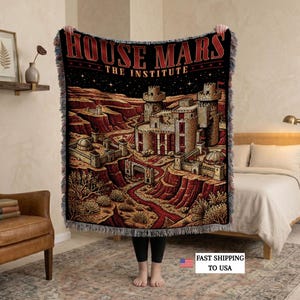 Könnte beinhalten: Eine gewebte Wohndecke mit einem dunklen Sternenhimmel über einer Wüstenlandschaft und einer steinernen Burganlage. Der Text HOUSE MARS THE INSTITUTE ist oben in Rot aufgedruckt. Die Decke hat einen Fransenrand und eine strukturierte Oberfläche.