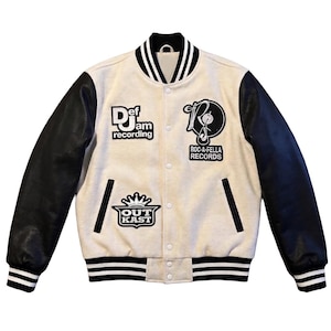 May include: Cream-colored varsity jacket with black leather sleeves. Features patches for Def Jam Recordings, Roc-A-Fella Records, and OutKast. The jacket has a black and white striped collar, cuffs, and hem.
