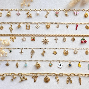 May include: Six gold-tone metal chains arranged horizontally, each featuring a variety of small charms including animals, flowers, symbols, and geometric shapes. The charms are crafted in various colours and finishes, hanging from the link chains.