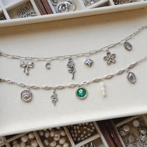 May include: Two silver-toned charm bracelets featuring various pendants including a bow, crescent moon, rose, star, flower, shell, paw print, snake, a green circular charm with a white flower, and a small strand of three white pearls.