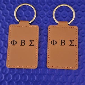 Könnte beinhalten: Handgefertigtes Holzschild mit dem Wort "Welcome" in verspielter Schrift. Es hat einen weißen, abgenutzten Hintergrund und einen dunkelbraunen Rand, ideal für eine Eingangstür oder einen Flur.