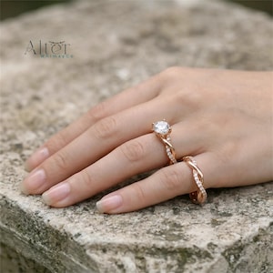May include: A rose gold ring set featuring a central round-cut clear stone on a twisted band and a matching twisted eternity band. Both rings are encrusted with small clear stones. The text Alter WhimsyCo is visible in the upper left corner.