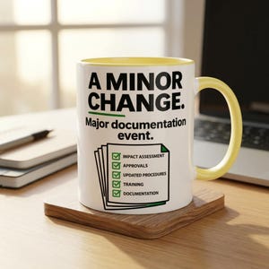 May include: A white ceramic mug with a yellow interior and handle. The front features black text reading A MINOR CHANGE. Major documentation event. Below is a graphic of a checklist with green checkmarks for impact assessment, approvals, updated procedures, training, and documentation.