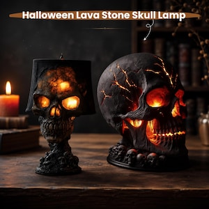 Könnte beinhalten: Zwei Halloween-Totenkopf-Lampen aus Lavastein mit dunklen, strukturierten Oberflächen. Die linke Lampe hat einen Totenkopf-Sockel mit schwarzem Schirm, während die rechte ein großer, rissiger Totenkopf ist, der warmes, oranges Licht ausstrahlt.