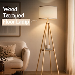 May include: A wooden tripod floor lamp with a white lampshade and a small shelf. The lamp has a light wood finish and a neutral-toned lampshade. The text "Wood Tetrapod Floor Lamp" is displayed on the image.
