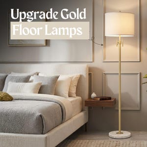 May include: A tall floor lamp with a brushed gold metal stand, a white cylindrical fabric shade, and a circular white marble base. The lamp features a pull chain switch and emits a warm glow. Text on the image reads Upgrade Gold Floor Lamps.