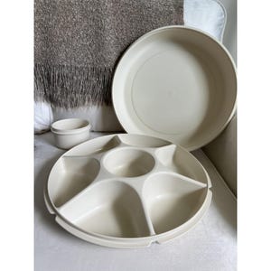 May include: A set of off-white serving dishes. The set includes a large round divided tray, a lid, and a small round container. The tray has five sections and a central dip area. The items are made of a durable plastic material.
