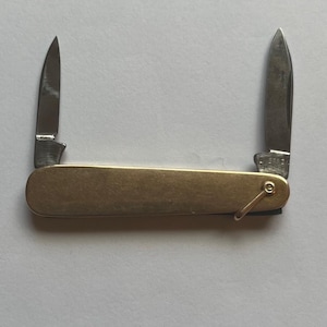 May include: A vintage pocket knife with two blades extended. The knife has a brass handle and a small ring for attachment. The blades are silver and show signs of wear. The knife is open, displaying the blades.
