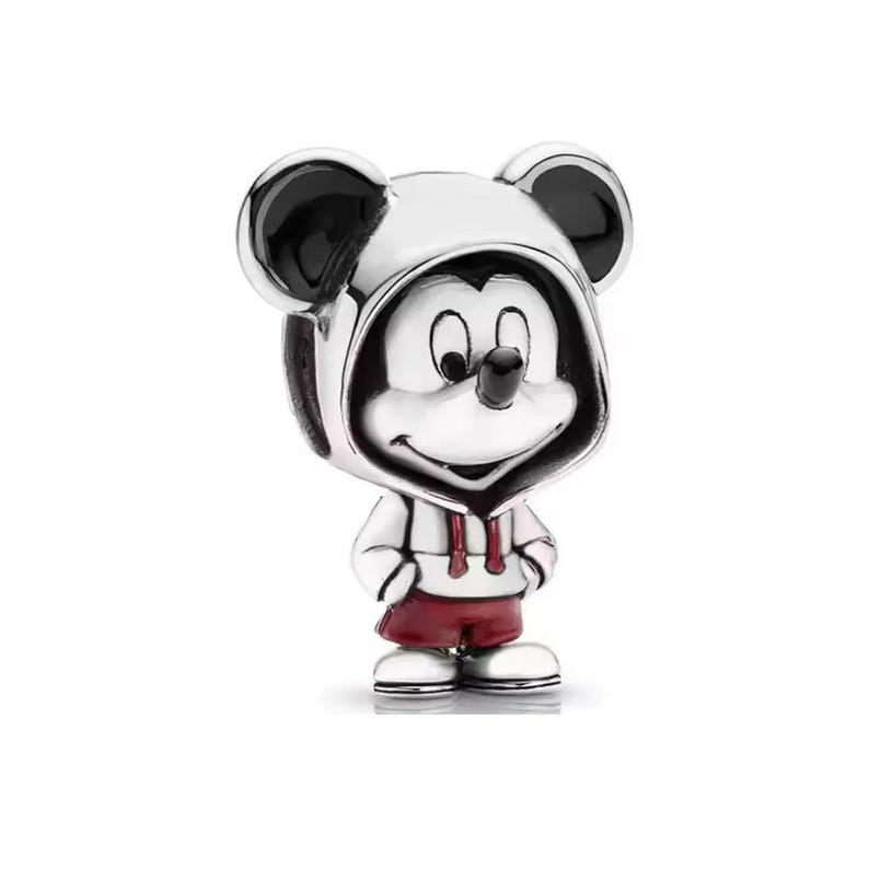 Puede incluir: Un charm plateado que representa a Mickey Mouse con una sudadera blanca con cord&oacute;n rojo y pantalones cortos rojos a juego. El charm tiene orejas negras y una cara sonriente, de pie con las manos a los lados.