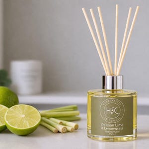 Può includere: Un diffusore a lamelle di vetro con lamelle di legno, etichettato "Persian Lime & Lemongrass". La bottiglia è accanto a lime fresche e citronella. Il diffusore è da 100 ml.