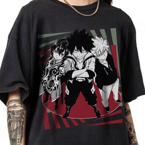 May include: Dark gray t-shirt featuring a graphic of three anime characters. The characters are in black and white, with a red and green background design. The characters are standing in a circle.