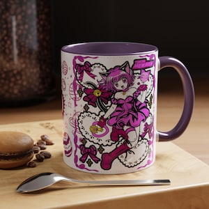 May include: A white ceramic mug with a purple interior and handle, featuring a graphic illustration of a pink-haired anime character in a purple outfit, bows, and the text Tokyo Mew Mew. The design includes decorative lace patterns and small stars.