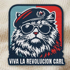 May include: Embroidered patch featuring a cat wearing sunglasses and a beret, with the text "VIVA LA REVOLUCION CARL". The patch has a blue, red, and white color scheme, with intricate stitching details.