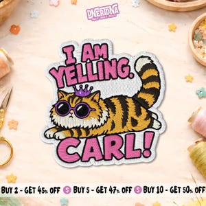 Peut inclure: Un écusson brodé représentant un chat touffu rayé orange et noir portant des lunettes de soleil violettes et une petite couronne violette. Le texte indique I AM YELLING. CARL! en lettres roses grasses avec un contour noir sur fond blanc.