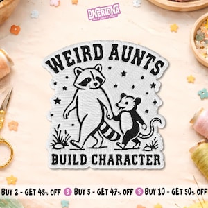 May include: A white embroidered patch featuring a black illustration of a raccoon and an opossum holding hands. The text WEIRD AUNTS BUILD CHARACTER is stitched in black above and below the animals, surrounded by small black stars and grass.