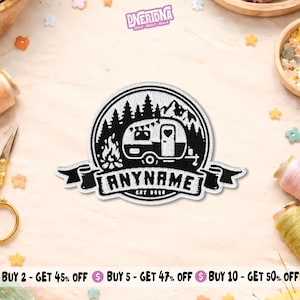 May include: A circular embroidered patch featuring a black and white design of a camping trailer, a campfire, and pine trees. A banner at the bottom contains the text ANYNAME and EST 2015. The patch has a white border and a detailed stitched texture.