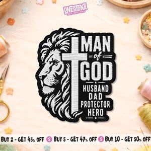 May include: Black and white embroidered patch featuring a lion's head and a cross. The text reads "MAN of GOD, HUSBAND, DAD, PROTECTOR, HERO". The patch has a detailed design and is likely for clothing or accessories.