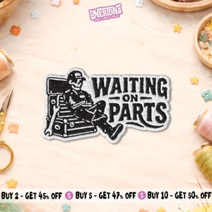 May include: An embroidered patch featuring a black and white design of a person sitting on a toolbox with the text WAITING ON PARTS. The patch has a white border and depicts a figure wearing a cap, leaning back with arms crossed.
