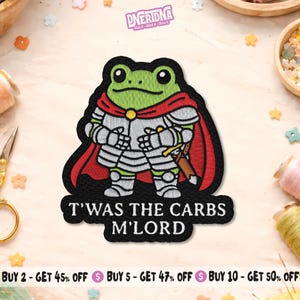 May include: Embroidered patch featuring a green frog in knight's armor with a red cape. The patch has the text "T'WAS THE CARBS M'LORD" in white. The patch is black with white, green, red, and silver details.