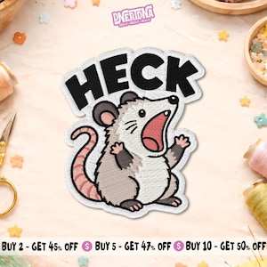 May include: An embroidered patch featuring a cartoon opossum with grey and white fur, a pink tail, and an open mouth. Above the opossum, the word HECK is stitched in bold black letters. The patch has a white border and a detailed thread texture.