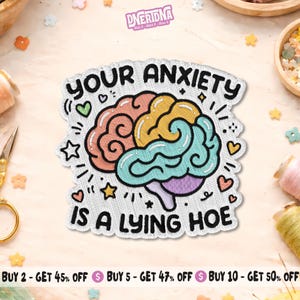 May include: An embroidered patch featuring a stylized brain divided into sections of pink, yellow, and teal. The text "YOUR ANXIETY IS A LYING HOE" is stitched in black around the brain, surrounded by small embroidered hearts and stars.