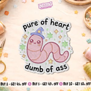 May include: Embroidered patch featuring a pink worm wearing a blue wizard hat, with the text "pure of heart dumb of ass". The patch is surrounded by stars and green shapes.