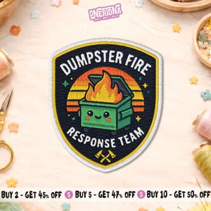 Peut inclure: Écusson brodé en forme de bouclier. Il représente une poubelle verte en feu, avec le texte "DUMPSTER FIRE RESPONSE TEAM". Le design comprend un fond de coucher de soleil jaune et orange et des haches croisées.