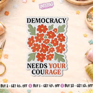May include: Embroidered patch with the words "DEMOCRACY NEEDS YOUR COURAGE" above a cluster of orange flowers and green leaves. The patch has a white background with a textured appearance.