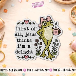 May include: An embroidered patch featuring a green frog wearing a pink bow, holding a pink mug with a heart, and standing near flowers. The text reads: first of all, jesus thinks i'm a delight. The patch is bordered by small pink hearts and vines.
