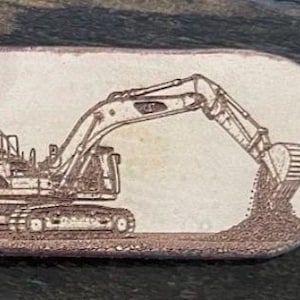 May include: An oval-shaped light tan keychain featuring a detailed laser-engraved illustration of a construction excavator digging into a pile of dirt. The keychain includes a silver-toned metal split ring attached through a hole on the left side.
