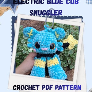 May include: An electric blue crochet cub snuggler with black and yellow accents. The plush toy has large black eyes and a pink nose. The image also includes the text "ELECTRIC BLUE CUB SNUGGLER" and "CROCHET PDF PATTERN BY:MARZZZYSCREATIONS."