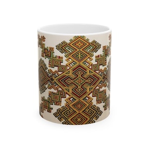 May include: White ceramic coffee mug featuring a repeating geometric pattern in shades of red, green, and gold on a cream background. The design is symmetrical and intricate, with a central diamond shape.
