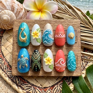 May include: A collection of ten artificial nails with a tropical theme. Each nail showcases a unique design, such as a gold hook, a flower, a wave, and a turtle. The nails are in various colours, including teal, white, red, and blue.